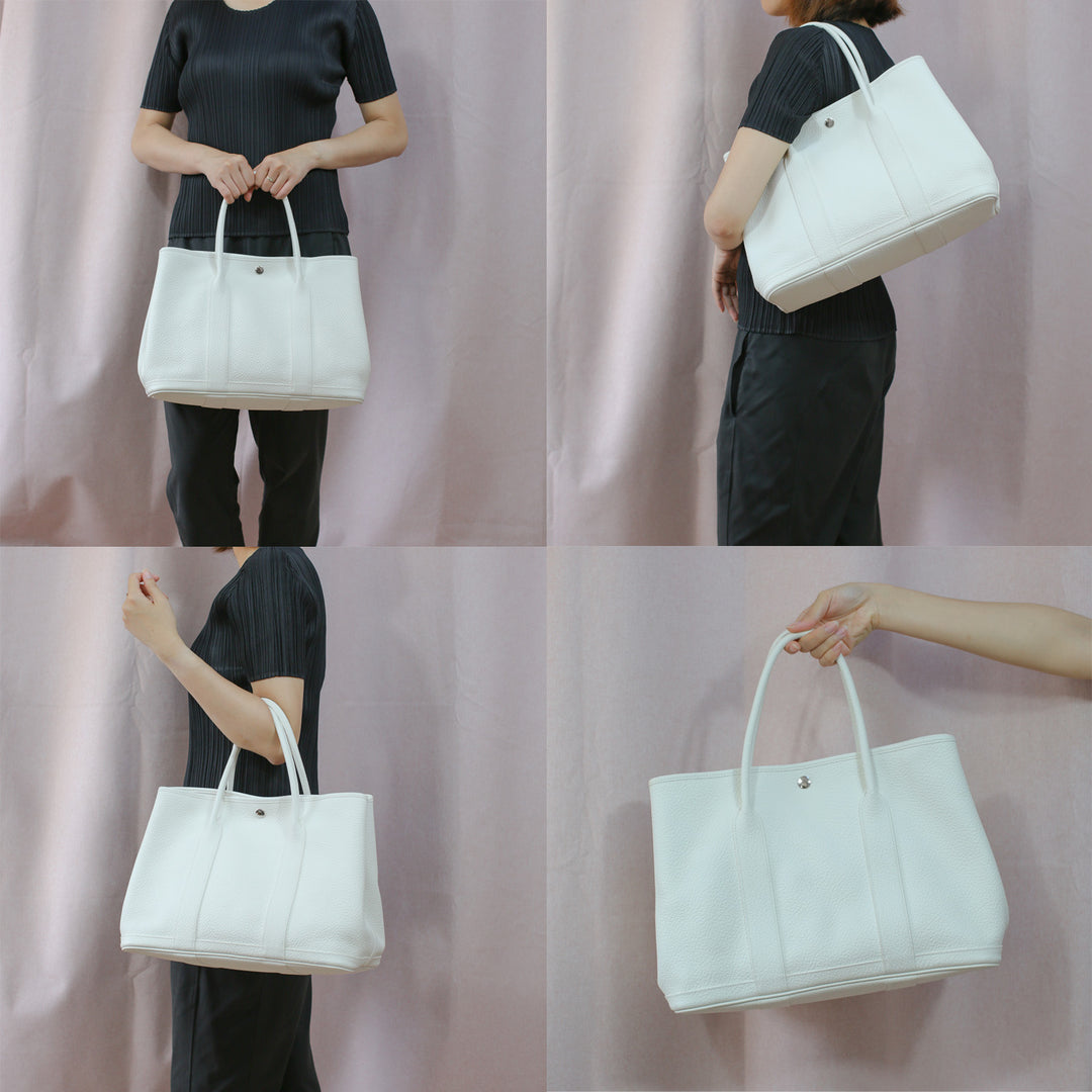 Model carrying the handbag by its handles as a top-handle bag and a shoulder bag.